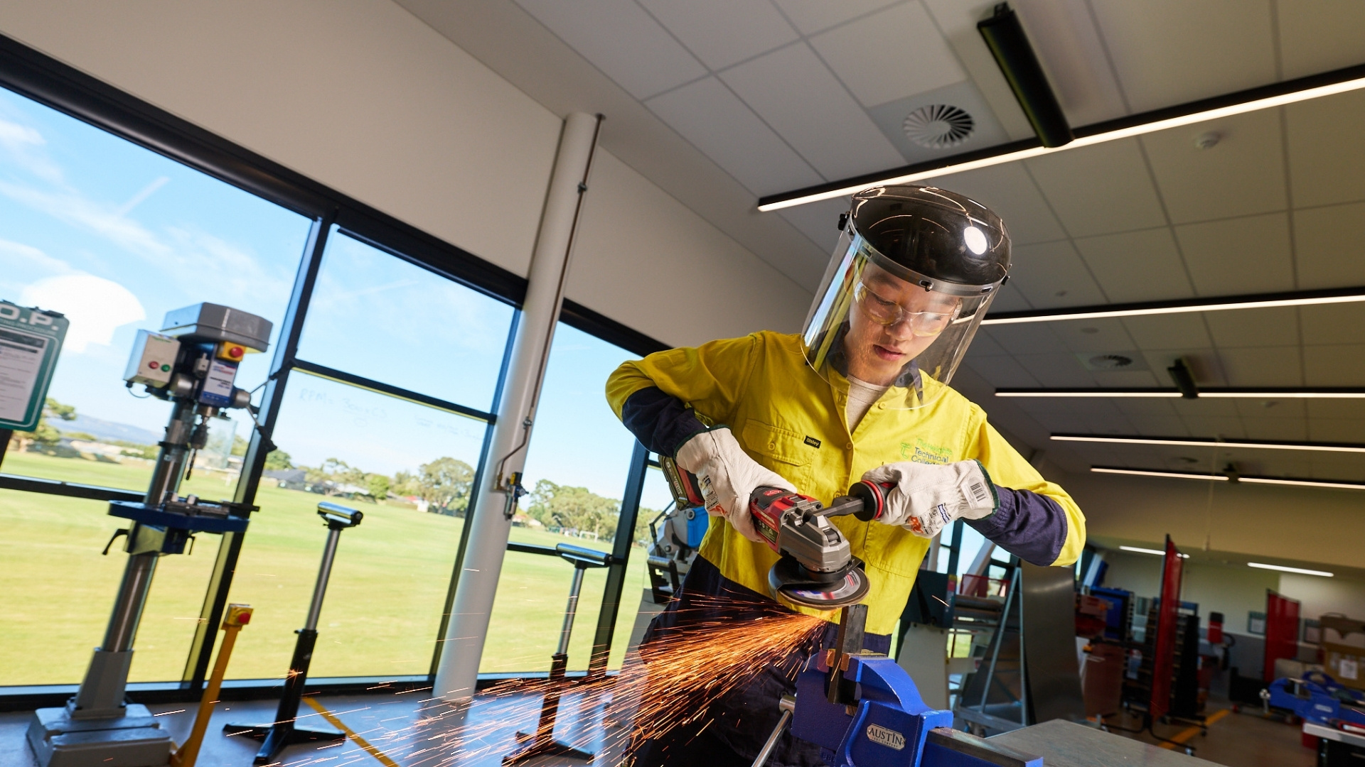 Advanced manufacturing student wearing protective equipment while using an angle grinder in a workshop.