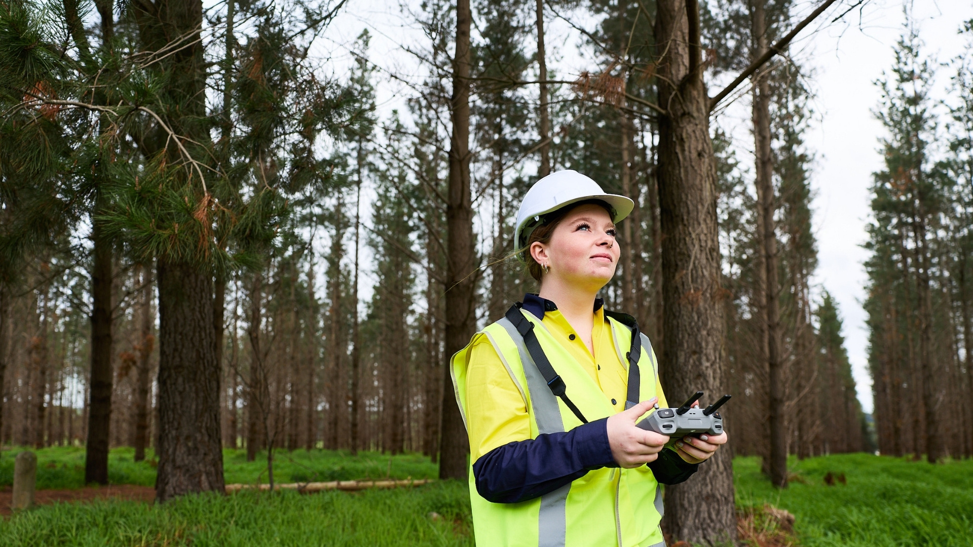Student operating a drone in a forest while wearing high-visibility PPE for agritech field training.