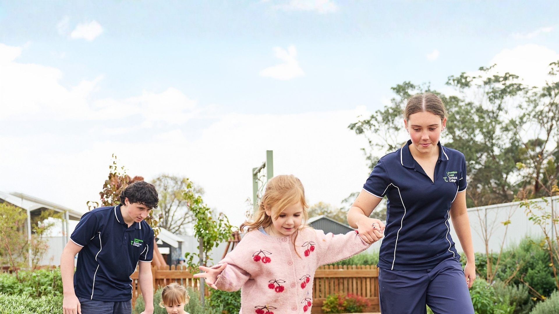 Early childhood students supporting young children during outdoor play in a learning environment.