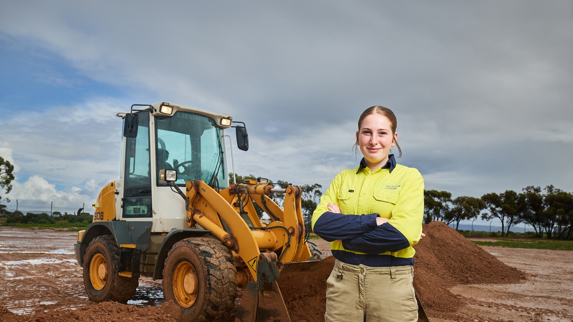 Civil construction student standing beside a front-end loader at a training site.