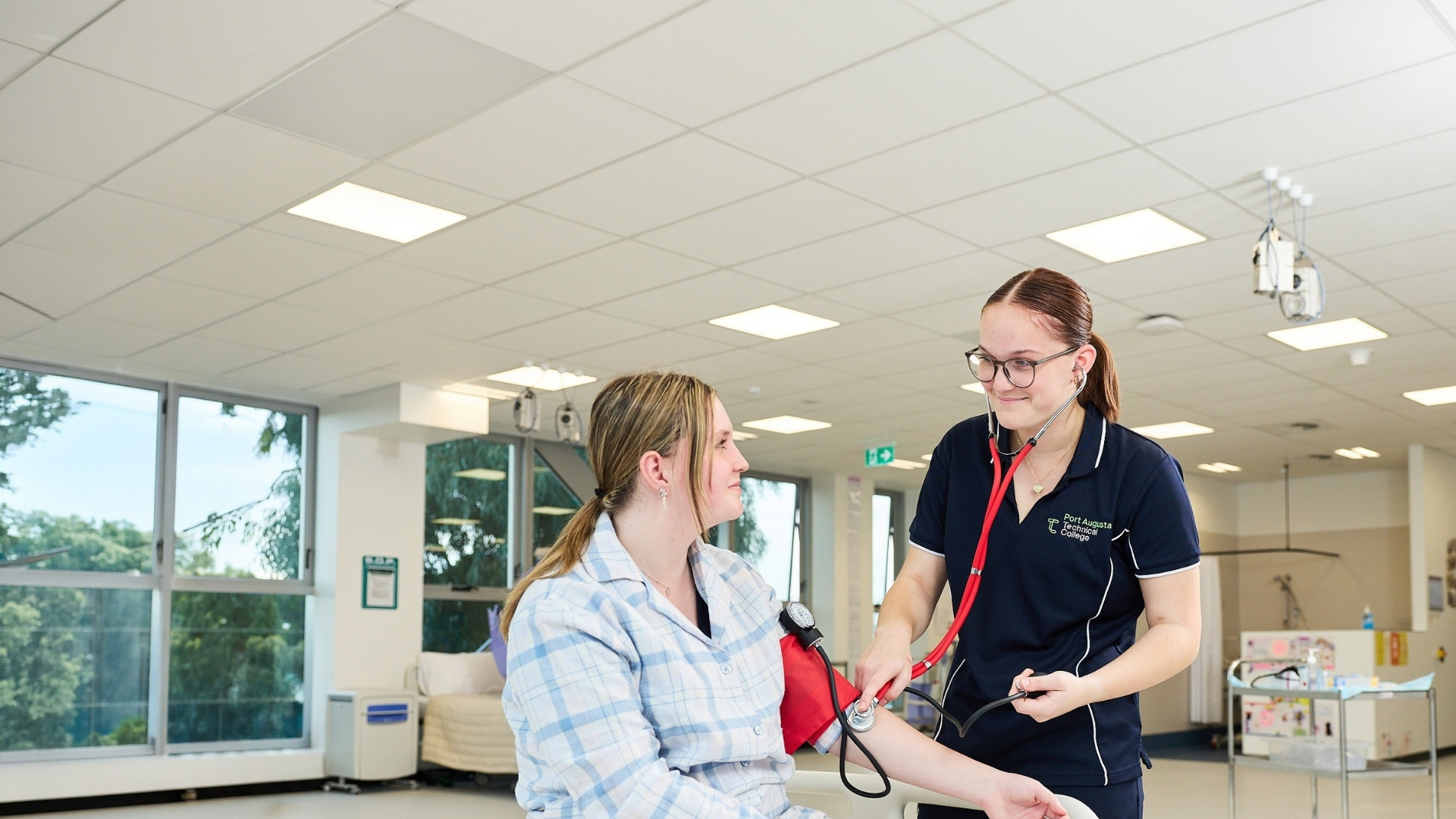 Health student taking a patient's blood pressure in a clinical training environment.