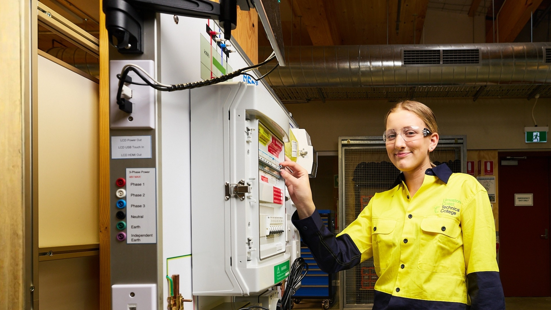 Multitrades student working on an electrical switchboard while wearing safety glasses and protective clothing.